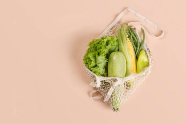 Yeşil sebzeler ve bej arka planda bitkilerle örülü ağ iplik torbası. Sürdürülebilir yaşam tarzı. Çevre dostu kavram. Üst Manzara. Boşluğu kopyala