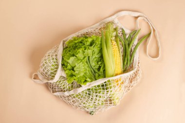 Yeşil sebzeler ve bej arka planda bitkilerle örülü ağ iplik torbası. Sürdürülebilir yaşam tarzı. Çevre dostu kavram. Üst görünüm.