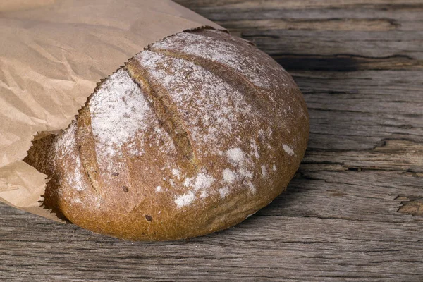 Round loaf of buckwheat bread in a paper bag on a wooden table.