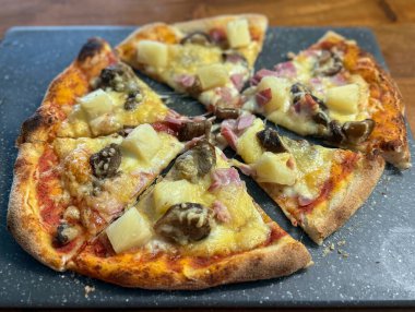 Homemade pizza with pineapple ham and mushrooms on a rustic board. Warm baked cheese creates an inviting comfort food mood.