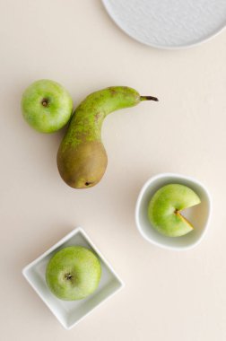 Tabakların, kaselerin, sulu elmaların ve parlak masanın üzerindeki armudun üst görüntüsü.