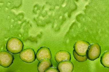 Islak yeşil yüzeyde taze salatalık dilimlerinin üst görüntüsü. Boş alan. Nemlendirici güzellik tedavileri.