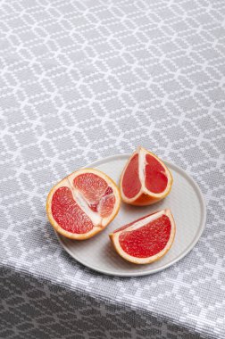Dikey görüntü. Gri tabakta greyfurt parçaları ve mutfak masasında masa örtüsü. Boş yer.
