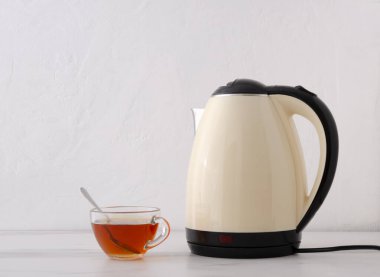 Cam fincan siyah çay ve beyaz duvara karşı parlak elektrikli su ısıtıcısı.