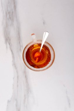 Dikey görüntü. Beyaz mermer masa üzerinde bir kaşık bal bulunan cam bardak siyah çay manzarası. Boş alan.