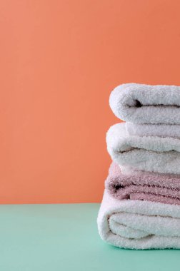 Mavi arka planda turuncu duvara dayalı temiz beyaz ve pembe havlular yığını. Boş alan.