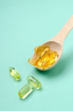 Dikey görüntü. Mavi yüzeyde ahşap kaşık ve sarı kapsüller.