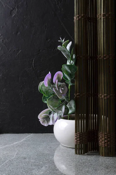 Vertical image.Eucalyptus leaves in the vase against straw board, grey table and dark wall.Empty space