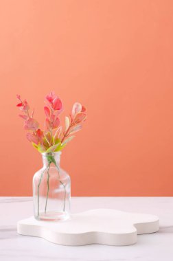 Dikey görüntü. Cam vazo ve beyaz podyum. Beyaz masada turuncu duvara karşı.