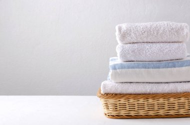 Beyaz masadaki hasır sepetteki temiz havlular parlak duvara karşı. Boş alan.