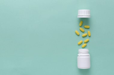 Sarı vitamin hapları ve açık bir şişe. Mavi yüzeyde bir fincan. Boş alan.