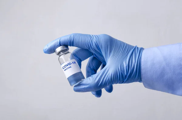 青い手袋を着用し 灰色の背景にワクチン用量のガラス瓶を保持医師 — ストック写真