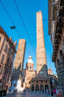 Bologna, Emilia-Romagna / İtalya - 20.08.2020: Bologna 'daki Garisenda ve Asinelli kuleleri çevresindeki binalar ve sokakta turistlerin bulunduğu bir geçidin ortasında