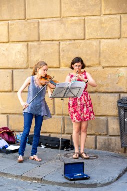 Siena, Toskana-İtalya - 08 / 27 / 2020: Birinde keman, diğerinde ise müzik aleti olan iki genç sokak müzisyeni para toplamak için enstrüman kutusuyla birlikte evin duvarının önünde müzik çalıyorlar.