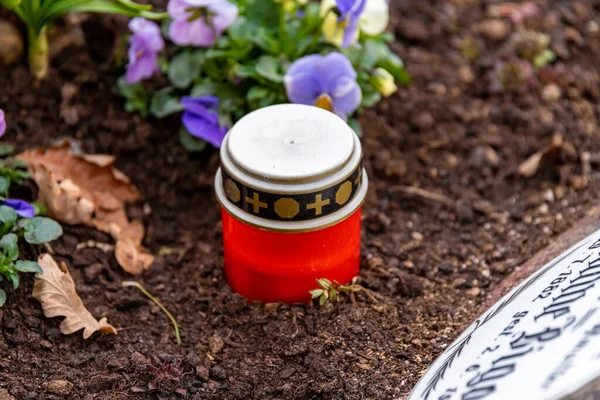 Kırmızı bir mum, kırmızı bir cam ve Hıristiyan süslemeleriyle kaplı bir kapakla çiçeklerin arasında yas tutan ışığı şekillendirdi..