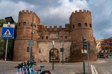 Rom - Lazio - İtalya - 08-21-2025: Bir yol kenarında seyyar atıştırmalık büfesi, içecekler ve paketlenmiş yiyeceklerle dolu bir şekilde açık dururken, bir kişi ağaçların altında ve bir lambanın altında dinleniyor.