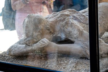 Pompei - Campania İtalya 08-25-2025: Pompei Harabeleri 'ndeki sütunlar arasında duran, tuğla duvar ve yeşil yapraklı bir kapı eşiğinde duran çıplak bir erkek figürün solmuş freski.