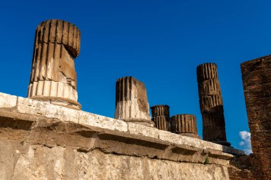 Pompei - Campania - İtalya - 08-25-2025: Güneşli kırık sütunlar Pompei harabelerinde taş bir duvarda duruyor, yıpranmış yüzeyleri açık mavi gökyüzüne karşı yükseliyor.