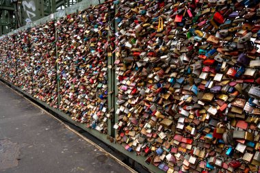 Koeln - Kuzey Ren-Vestfalya - Almanya - 11-02-2024: Binlerce renkli asma kilit, kaldırım kenarındaki bir köprüyü örterek, birbirine bağlı aşk kilitlerinin yoğun dokulu bir görüntüsünü oluşturuyor.
