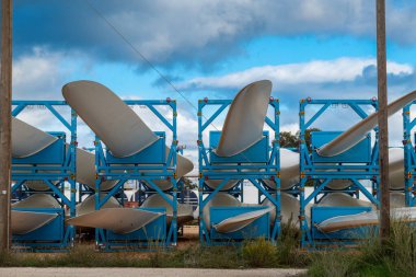 Preveza - Epirus - Yunanistan - 10-18-2025: Türbin ucu, bir deponun önünde, yol kenarında ve uzun rafların arkasında kırılmış bulutlarla mavi çelik çerçevelerde oturuyor.