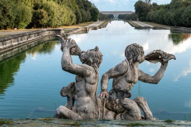 Reggia di Caserta - Campania - İtalya - 08-30-2025: Caserta Kraliyet Sarayı 'na giden kanal kenarında deniz kabuğu ve boynuz üfleyen mitolojik heykeller.