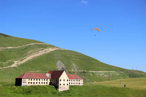 hang glider and a house with a red roof in the mountains