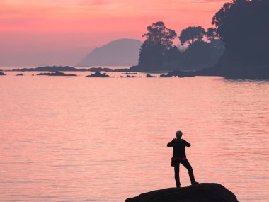 unrecognizable person taking photo with mobile at sunset on a rock to the cies islands in spain
