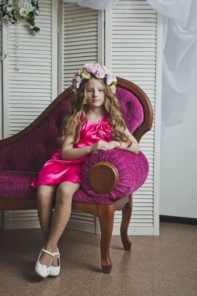 Bambina in una ghirlanda di fiori lilla seduta sul divano 602 — Foto Stock