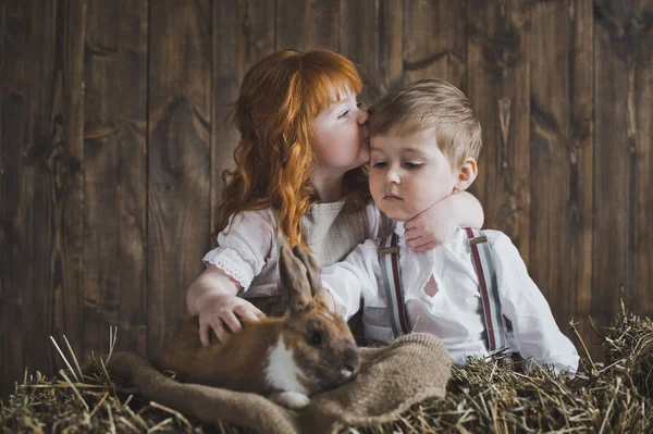 Roodharige meisje en jongen spelen met het konijn in het hooi 6123. — Stockfoto