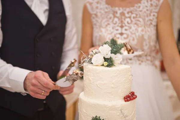 新鮮な花や小枝で飾られた結婚式の白いケーキは 花嫁と新郎の背景に立っています — ストック写真