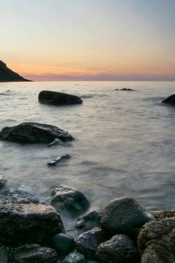 Denizde siyah kayalar. Gün batımlı temiz sahil şeridi. uzun pozlama fotoğrafı