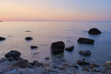 Denizde siyah kayalar. Gün batımlı temiz sahil şeridi. uzun pozlama fotoğrafı