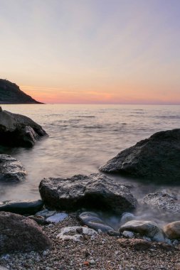 Uzun kepenk, açık sisli kıyı şeridi ve denizde kayalar var.