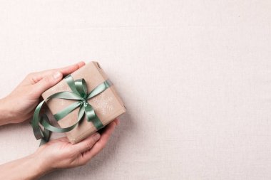 Kadın elleri, arka planda kurdele ışığı arkaplan görünümlü bayram kutusunu tutuyor.