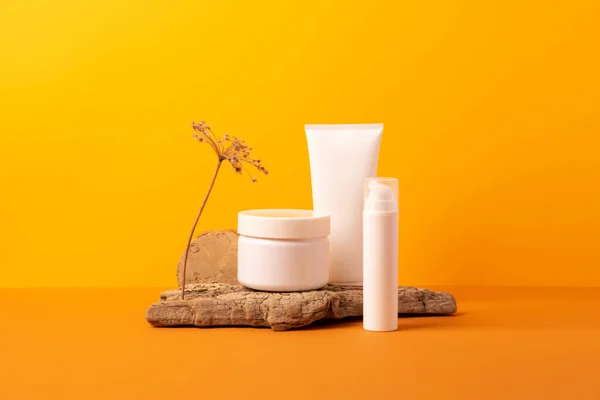 Group of cosmetic tubes bottles podium from natural materials orange background