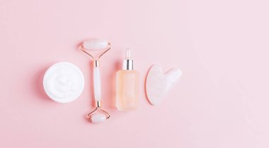 Yüz masajı seti silindir kazıyıcı guasha pembe arka plan.