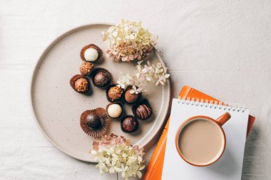 Bir fincan kahve. Masadaki seramik tabakta çeşitli çikolatalardan bir kutu iç.
