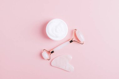 Yüz masajı seti silindir kazıyıcı guasha pembe arka plan.