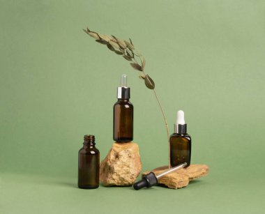 Doğal malzeme taşlarından yapılmış soyut bir podyumda bir şişe serum yağı kozmetik maddesi yeşil pastel arka plan.