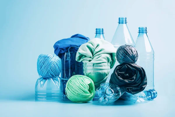 Boş plastik şişe ve geri dönüştürülmüş polyester liften yapılmış çeşitli kumaşlar mavi arka planda sentetik kumaş.