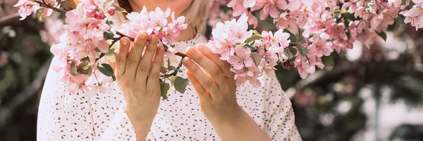 Las manos de las niñas están sosteniendo una rama en flor con flores rosadas delicadas sueltas. Concepto primavera verano naturaleza flores — Foto de Stock