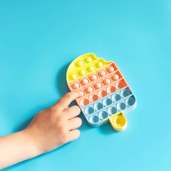 Toque na moda brinquedo brilhante antistress pop-lo em crianças mãos azul fundo espaço de cópia — Fotografia de Stock