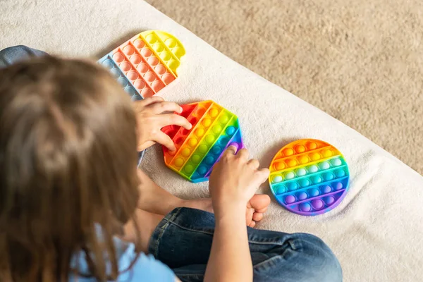 As mãos das crianças jogam um brinquedo pop anti-stress sensorial na moda. A criança brinca com um brinquedo de silicone com bolhas suaves — Fotografia de Stock