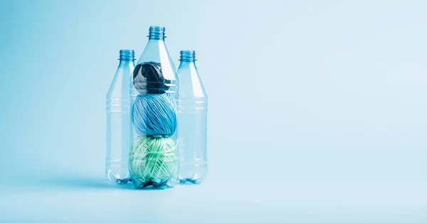 Plastik geri dönüşüm ve yeniden kullanma konsepti. Boş plastik şişe ve polyester fiber iplik mavi arka planda..