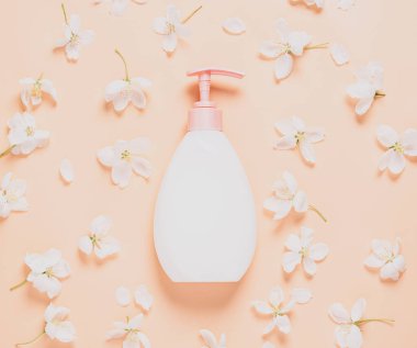 Vücudunu ve yüzünü nemlendirmek ve bakımını sağlamak için taze çiçeklerin arka planına karşı bir şişe sıvı sabun kremi.