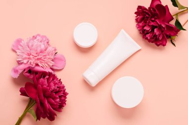 Kozmetik ürünleri krem jöle şampuan çeşitli şişelerde pembe arka planda taze çiçek şakayıkları
