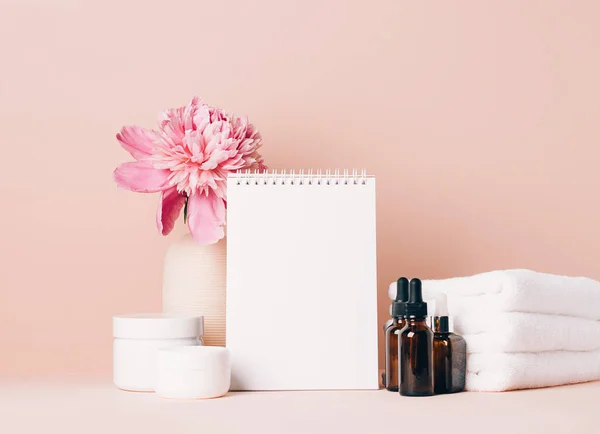 Los accesorios para mujer el aceite de crema los cosméticos distintos limpian el cuaderno en blanco sobre la mesa con las flores. Concepto de belleza — Foto de Stock