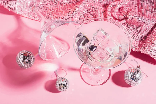 Martini mit Eis in einem eleganten Glas Discokugeln auf einem glänzend rosa Hintergrund. Modisches helles direktes Blitzlicht. — Stockfoto