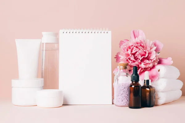 Los accesorios para mujer el aceite de crema los cosméticos distintos limpian el cuaderno en blanco sobre la mesa con las flores. Concepto de belleza — Foto de Stock