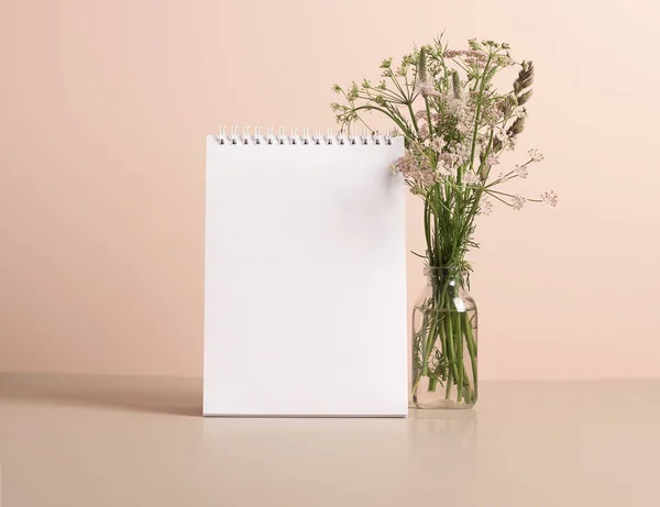 Los planificadores en blanco bloc de notas limpio se encuentra en la mesa en jarrón con delicadas flores verdes. Prepárate para el texto —  Fotos de Stock